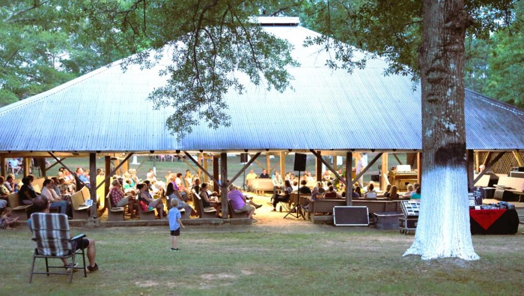 People gathering under a large pavilion in a park.